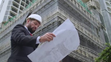 İnşaat alanındaki bir mühendis, bir müteahhit, çizimleri, binanın ne aşamada olduğunu kontrol eder, çizimlere bakar, ve sonra binaya bakar..
