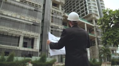 Yüz koruyucu maske takan mühendis erkek mühendisler binanın planlarını tutuyor ve Corona virüsünün COVID 19 salgını veya salgını sırasında inşaat sahasının altında çalışıyor..
