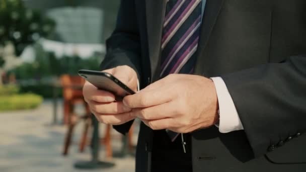 대도시 금융 지구의 고급 옷을 입은 중년 사업가가 휴대폰을 사용하여 문자 메시지를 보내고 있다. — 비디오