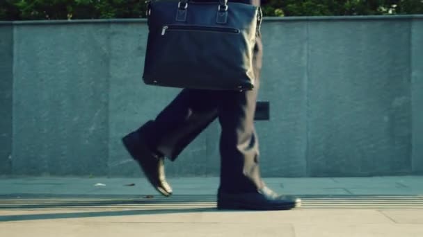 İş adamının işe giderken bacaklarının arkası görünüyor. Orta yaşlı beyaz bir işadamının güneşli bir yaz gününde kaldırımda yürümesini yakından çek.. — Stok video