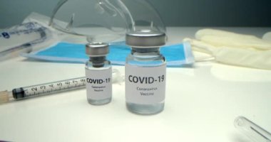 COVID-19 'a karşı aşı, koronavirüs aşısı olan bir ampul ve yakınlarda çeşitli şırıngalar, tıbbi gereçler, koruyucu maske, Amerikan bayrağı ve kitaplarının geçmişi geliştirildi.