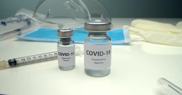 COVID-19 'a karşı aşı, koronavirüs aşısı olan bir ampul ve yakınlarda çeşitli şırıngalar, tıbbi gereçler, koruyucu maske, Amerikan bayrağı ve kitaplarının geçmişi geliştirildi. — Stok video