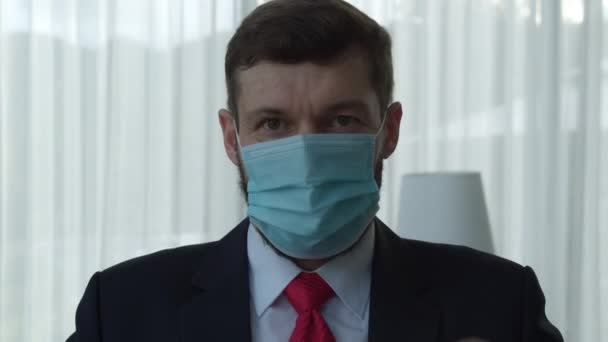 사무실에 앉아 카메라를 보고 열렬 한 보호를 위해 의료용 마스크를 벗고 있는 잘생긴 수염을 한 고위 사업가의 모습. — 비디오