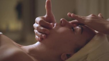 Spa yatağında uzanan güzel beyaz bir kadın güzellik salonundaki masaj terapistinden aroma esanslı yağ cildiyle yüz masajı yaptırıyor. Sağlık hizmeti vücut masajı spa konsepti.