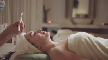 Spa yatağında uzanıp yüz masajı yapan rahat bir kadın lüks spa merkezindeki masör, spa merkezinde yüz maskesi takan bir kız. Sağlık, stres atma ve gençleştirme kavramı.