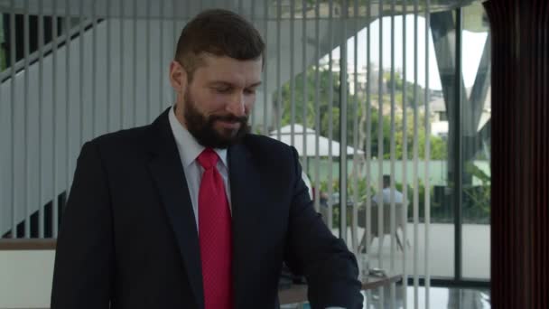 Hombre de negocios senior con barba en un traje de negocios, un director ejecutivo con una maleta en sus manos está en la recepción esperando a un administrador.El hombre de negocios barbudo mira su reloj de pulsera — Vídeos de Stock