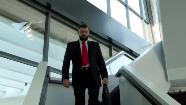 Netter kaukasischer Mann, Vorstandsvorsitzender kommt die Treppe im Büro eines modernen Unternehmens herunter, bärtiger Unternehmer CEO oder Manager mit einer Tüte voller Ideen die Treppe hinunter. — Stockvideo