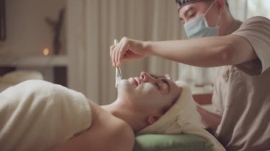 Spa yatağında uzanıp yüz masajı yapan rahat bir kadın lüks spa merkezindeki masör, spa merkezinde yüz maskesi takan bir kız. Sağlık, stres atma ve gençleştirme kavramı.