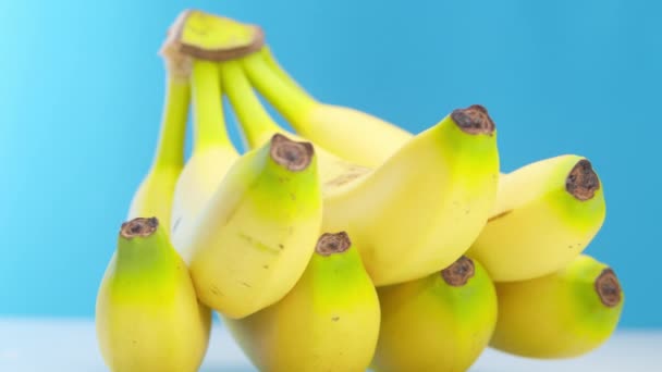 As bananas amarelas maduras bonitas com baixas da frescura encontram-se na mesa em um fundo azul. As bananas maduras giram em círculo. Ângulo interessante, imagens de estoque. — Vídeo de Stock