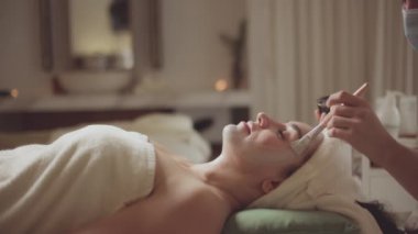 Rahatlamış bir kadın masaj terapisti tarafından yüz masajı ve spa tedavisi için spa yatağında yatıyor. Yüz bakımı yenileniyor. Güzellik salonunda kaldırma terapisi masajı yaptıran bir manken..