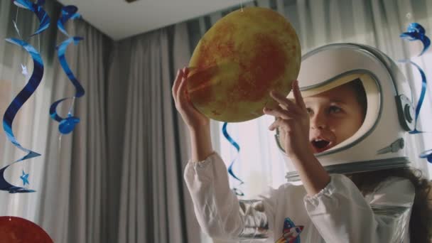 Mädchen Astronautin in Form eines Hummeln Astronautenkostüms spielt einen Raum in ihrem Kinderzimmer, Innenraum ist mit Planeten aufgehängt.Fantasie-Kind Astronautin spielt mit schwebenden kosmischen Planeten.