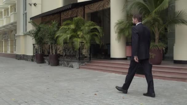Een senior zakenman met een baard in een duur pak en stropdas loopt met een aktetas in zijn handen op straat. — Stockvideo