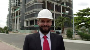 Potrait Kıdemli Mühendis Planlama Üretim Üretimi Beyaz koruyucu başlıklı bir iş elbisesi içinde şehrin yeni bir küçük bölgesinde yapılan bir inşaatı kontrol ediyor..