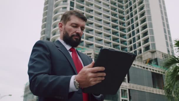 Man professioneel typen op een laptop toetsenbord in een straat. Portret van een positieve zakenman die naar het tabletscherm kijkt. Serieuze bebaarde zakenman werkt op tablet computer in het park. — Stockvideo