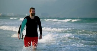 Sahilde sörf tahtası taşıyan yakışıklı yaşlı bir sporcunun portresi. Emekli bir sporcu denize girer, sörf tahtasıyla dalgalara biner..