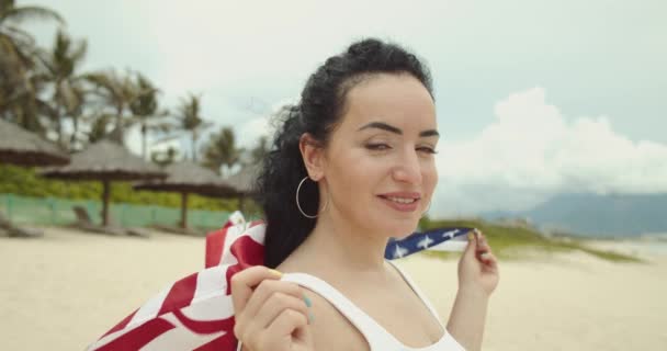 Patriotismo, día de la independencia y el concepto de días festivos - feliz joven sonriente en traje de baño con bandera nacional americana en la playa de verano. — Vídeo de stock