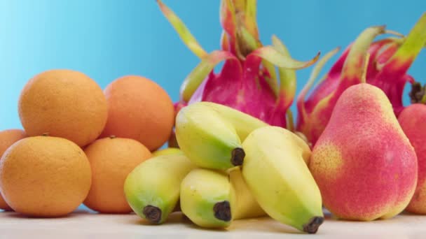 Čerstvé zdravé ovoce, jablka, pomeranče, banány, hrušky, dračí ovoce na modrém pozadí leží na bílém kuchyňském stole. Zdravý stravovací koncept, zdravý životní styl, veganská dovolená. — Stock video