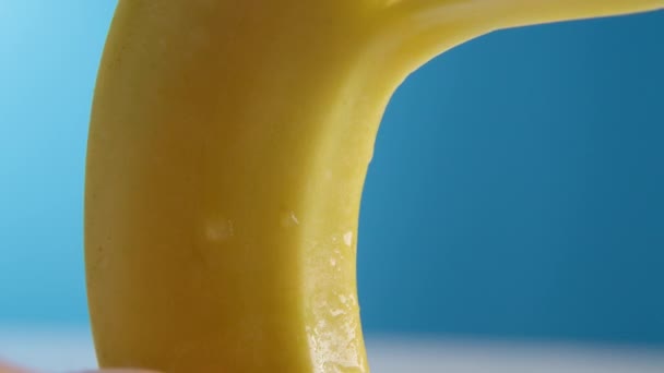 Макро-об'єктив знімає Свіжий банан пісяє на синьому фоні. Жіноча рука повільно видаляє або видаляє шкіру банана, концепцію фруктів, очищає банан . — стокове відео