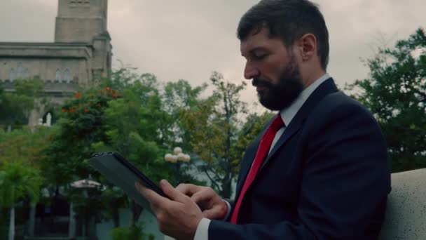 Olgun bir iş adamı parkta bankta oturmuş gazete okuyor. Şehirdeki merdivenlerde oturan gazete ve tablet bilgisayarlı iş adamları. — Stok video