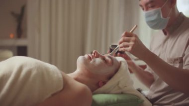 Spa yatağında uzanıp yüz masajı yapan rahat bir kadın lüks spa merkezindeki masör, spa merkezinde yüz maskesi takan bir kız. Sağlık, stres atma ve gençleştirme kavramı.