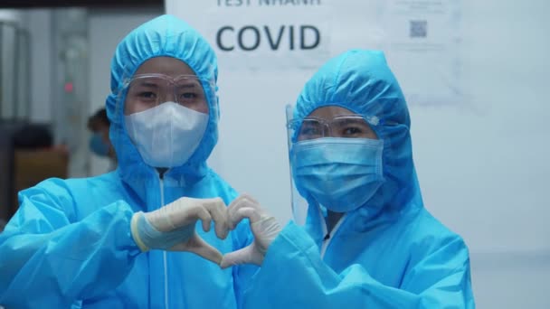 Lekarze w kombinezonach ochronnych podczas epidemii wykazują oznaki życia i serca na poparcie innych osób, które mogą być chore lub zakażone koronawirusem. — Wideo stockowe
