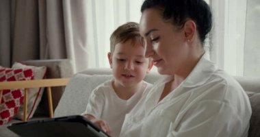 Mutlu anne ve tatlı oğul, küçük çocuk, anne bebeğiyle evde oynuyor, rahatlıyor, akıllı telefon kullanıyor, sarılıyor, kanepeye oturuyor, çocuk, komik videolar izliyor, eğleniyor, aile hayatının tadını çıkarıyor..