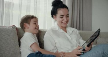 Mutlu anne ve tatlı oğul, küçük çocuk, anne bebeğiyle evde oynuyor, rahatlıyor, akıllı telefon kullanıyor, sarılıyor, kanepeye oturuyor, çocuk, komik videolar izliyor, eğleniyor, aile hayatının tadını çıkarıyor..