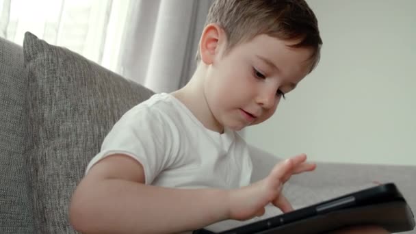 1人でカーペットフロアに寝そべっているデジタルタブレット技術デバイスを使用して好奇心旺盛なかわいい就学前の男の子。小さな子供は自宅でパッドコンピュータサーフィンインターネットプレイゲームを保持しています。子供技術中毒の概念 — ストック動画