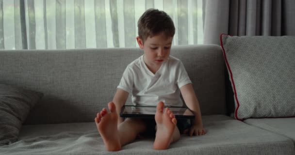호기심많고 귀여운 미취학 아동 이 카펫 바닥에 홀로 놓여 있는 디지탈 태블릿 기술 장치를 사용하고 있습니다. 어린이는 패드 컴퓨터 서핑을 집에서 하고 있다. 어린이 기술 중독 개념 — 비디오