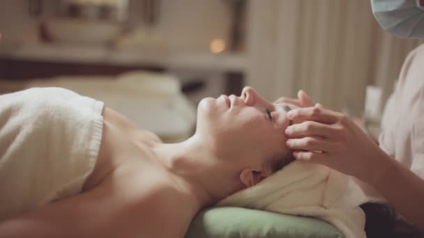 Bienestar salud masaje corporal concepto de spa. Joven hermosa mujer caucásica tumbada en la cama de spa obtener tratamiento de masaje facial con aroma aceite esencial cuidado de la piel de terapeuta de masaje en el salón de belleza. — Vídeos de Stock