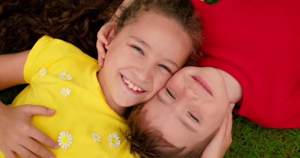 Happy little brother and sister lies on green grass. Children is dream on the grass in park. Happy face of baby. Little boy and girl looks at sky. Smile of Children and look up to camera — Stock Video