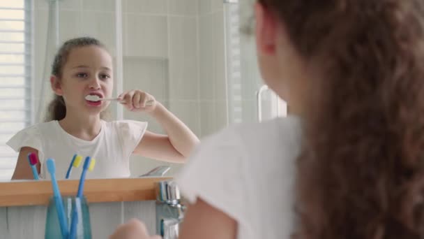 Портрет счастливый милый молодой девушки-подростка чистить зубы в ванной комнате и улыбаясь. Ежедневная медицинская помощь детям. Белый парень с белым зубом смотрит на изолированное зеркало. Стиль жизни. — стоковое видео