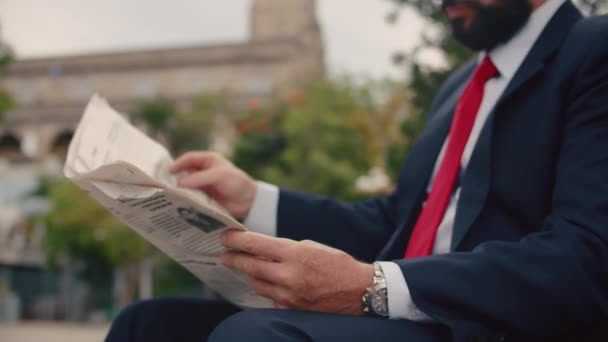 公園のベンチに座って新聞を読む黒の青いジャケットの美しい髭を生やした高価なスーツのビジネスマンシニア. — ストック動画