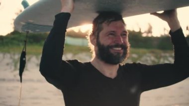 O yaştaki son sınıf sporcusu plajda sörf tahtasıyla gezer. Emekli bir sporcu denize açılır, dalgalara sörf tahtası ile biner..