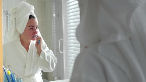 Šťastná mladá žena držící kartáček na zuby a dívající se do zrcadla. Krásná dívka čištění úst dělat ranní zubní péče rutina v koupelně, při pohledu na zrcadlo s ručníkem na hlavě. — Stock video