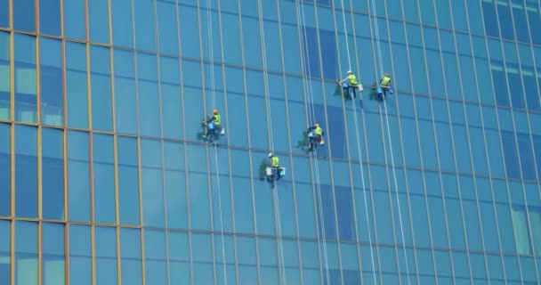 Öt férfi munkások piros és sárga munkaruhában takarítás a külső ablakok egy üzleti felhőkarcoló - ipari alpinizmus.high-rise emberek mossa ablakok.Koncepció takarítás — Stock videók