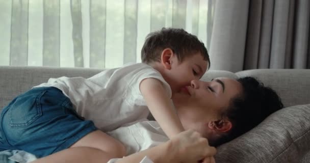 Een gelukkig gezin van moeder en zoon, samen op de bank rustend, slapen deze kleuters op hun moeders buik, knuffelen thuis, de moeder streelt het kind op het hoofd. — Stockvideo