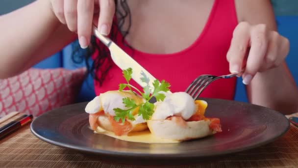 Couteau de gros plan extrême et une fourchette dans les mains d'une femme avec une manucure brillante coupent un œuf poché décoré de filets un saumon rouge, fille avec un couteau et une fourchette coupe un œuf poché. — Video