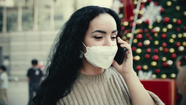 Ung vacker flicka i varma kläder står nära julgranar och talar via telefon på gatan. Sakta i backarna. Kvinnan talar i telefon nära julgranen. — Stockvideo