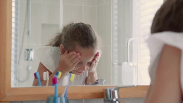 Портрет щасливої дівчини-підлітка, яка миє обличчя у ванній кімнаті та посміхається. Кавказька дівчинка з дзеркалом розмиває обличчя на самоті. — стокове відео