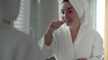 Oral Bakım Konsepti. Beyaz dişli, beyaz dişli beyaz kadın, evde izole edilmiş aynaya bakıyor. Banyoda dişlerini fırçalayan ve gülümseyen sevimli genç kız. Yaşam biçimi.