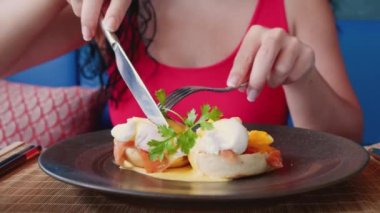 Son derece yakın çekim bıçağı ve parlak manikürlü bir kadının elindeki çatal, filetoyla süslenmiş haşlanmış bir yumurtayı, kırmızı somonla süslenmiş kırmızı somonu, çatallı ve bıçaklı bir kız haşlanmış yumurtayı kesiyor..