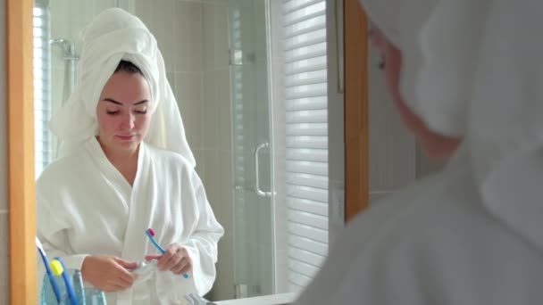 Begreppet munvård. Vit kvinna med vit tand tittar på spegeln isolerad hemma. Porträtt glad söt ung tonåring flicka borsta tänderna i badrummet och ler. Livsstil. — Stockvideo