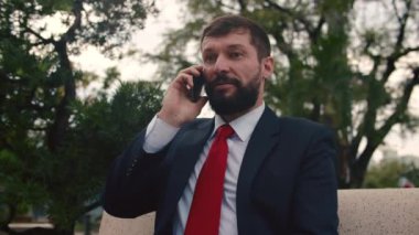 Gözlüklü Yakışıklı Sakallı İş Adamı cep telefonu kullanıyor. Parkta bir bankta otururken akıllı telefondan konuşan genç adam. İş için. Sosyal ağ. İnsanlar.