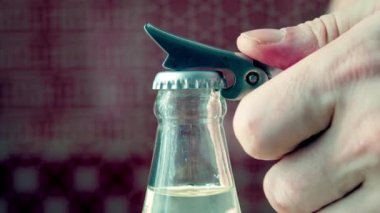 Bir adamın eli kapalı bir mutfakta bir şişe maden suyu ve bir şişe açacağı açar. Yavaş çekim