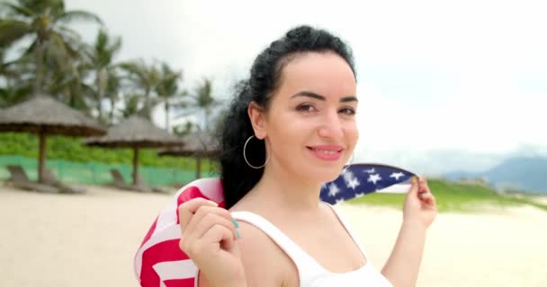 Patriotismo, independência dia e feriados conceito - feliz sorrindo jovem em maiô com bandeira nacional americana na praia de verão. — Vídeo de Stock