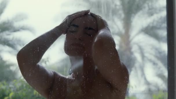Ung kvinna som duschar. Vacker flicka tvätta håret och njuta av en uppfriskande dusch, närbild porträtt. Baksidan syn på kvinnan i baddräkt tar regndusch, tropisk grönska på bakgrunden. — Stockvideo