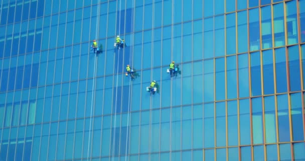 Bir iş gökdeleninin dış camlarını temizleyen kırmızı ve sarı elbiseli beş işçi. Endüstriyel dağcılık. Yüksek katlı insanlar camları siler. — Stok video