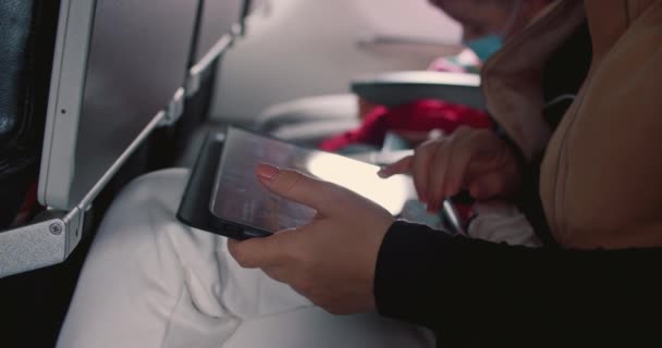 Eine junge Frau kaukasischen Aussehens fliegt im Flugzeug, ein Teenager benutzt ein Handy im Flugzeug, blättert durch Bilder, Nachrichten, öffnet eine Anwendung.