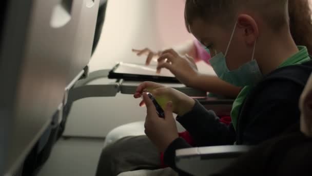 Crianças caucasianas em avião com máscara médica protetora.Menino e menina turista em avião com respirador jogar no telefone celular smartphone. Epidemia de coronavírus sars-cov-2 covid-19 2019-ncov. — Vídeo de Stock